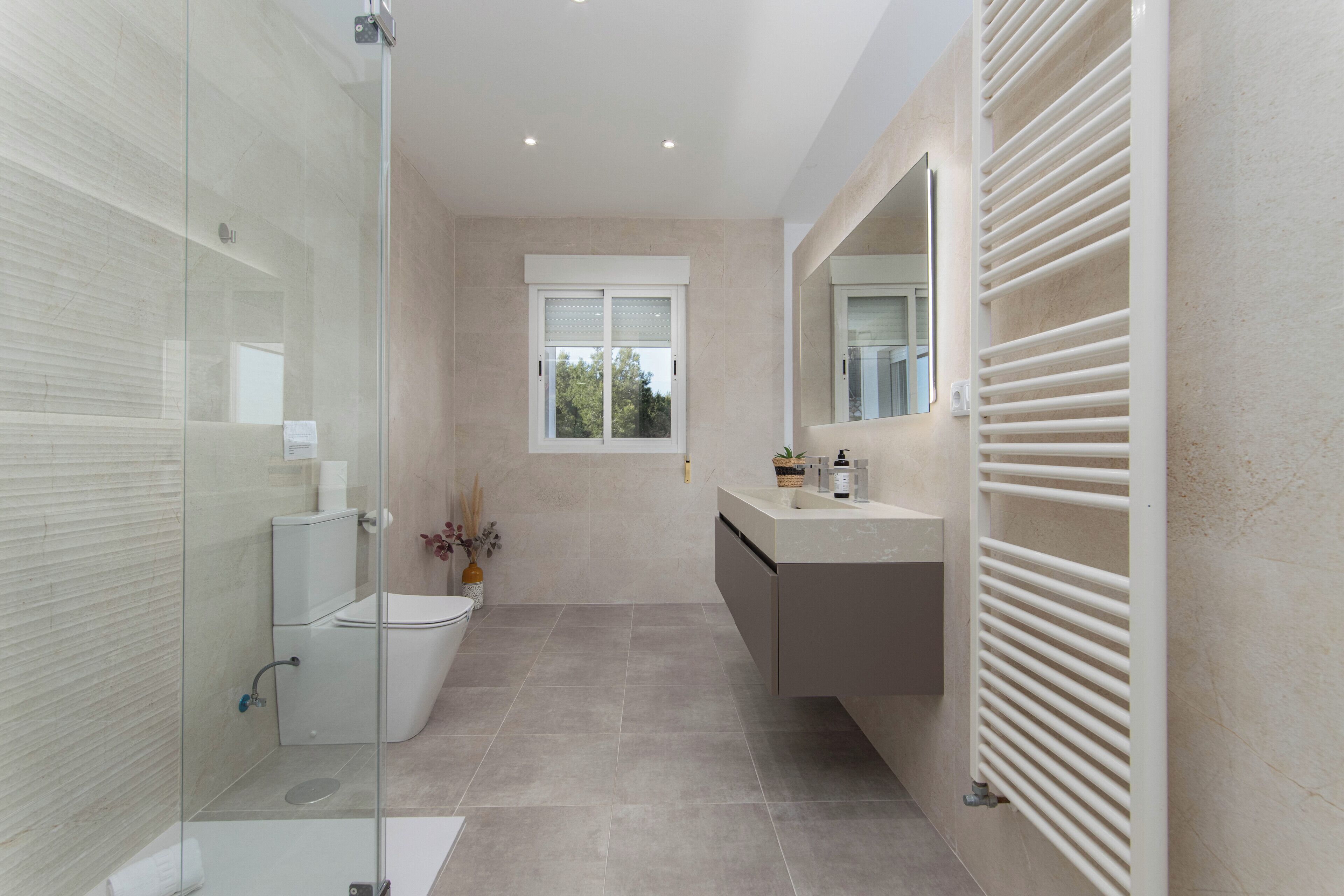 A modern bathroom with a glass shower enclosure, a toilet, a sink with a mirror, and a window.