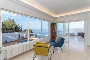 A spacious room with large windows, a yellow chair, a blue armchair, and a view of the sea.