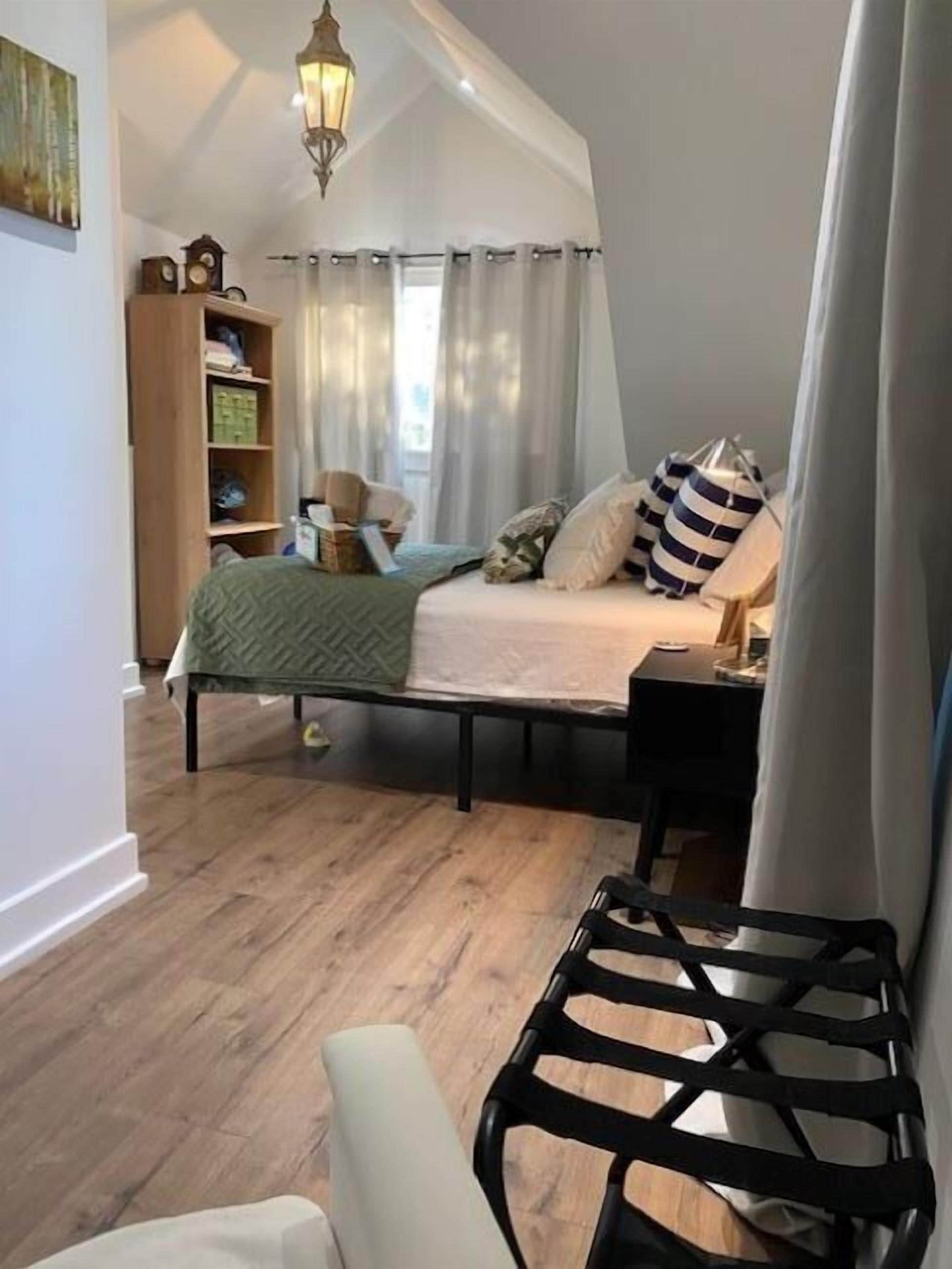 Ein Schlafzimmer mit Stockbett, Holzboden, Nachttisch, Sessel und Bücherregal.