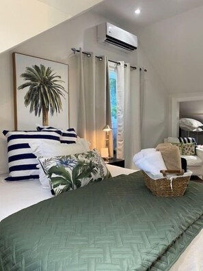 Un dormitorio con cama, almohadas, lámpara, aire acondicionado instalado en la pared y ventana con cortinas.