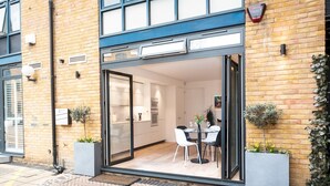 Un apartamento moderno con entrada por puerta de vidrio, un comedor con mesa y sillas, y una cocina visible a través de la puerta.