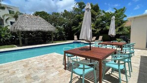 A poolside area with a thatched-roof structure, outdoor seating with umbrellas, and a clear blue sky. - 3/3 Duplex for 6+Shared Heated Pool, Tiki Bar BBQ (Hollywood)