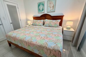 Une chambre à coucher avec un lit en bois, une literie à motifs floraux, deux lampes fixées au mur et une porte.