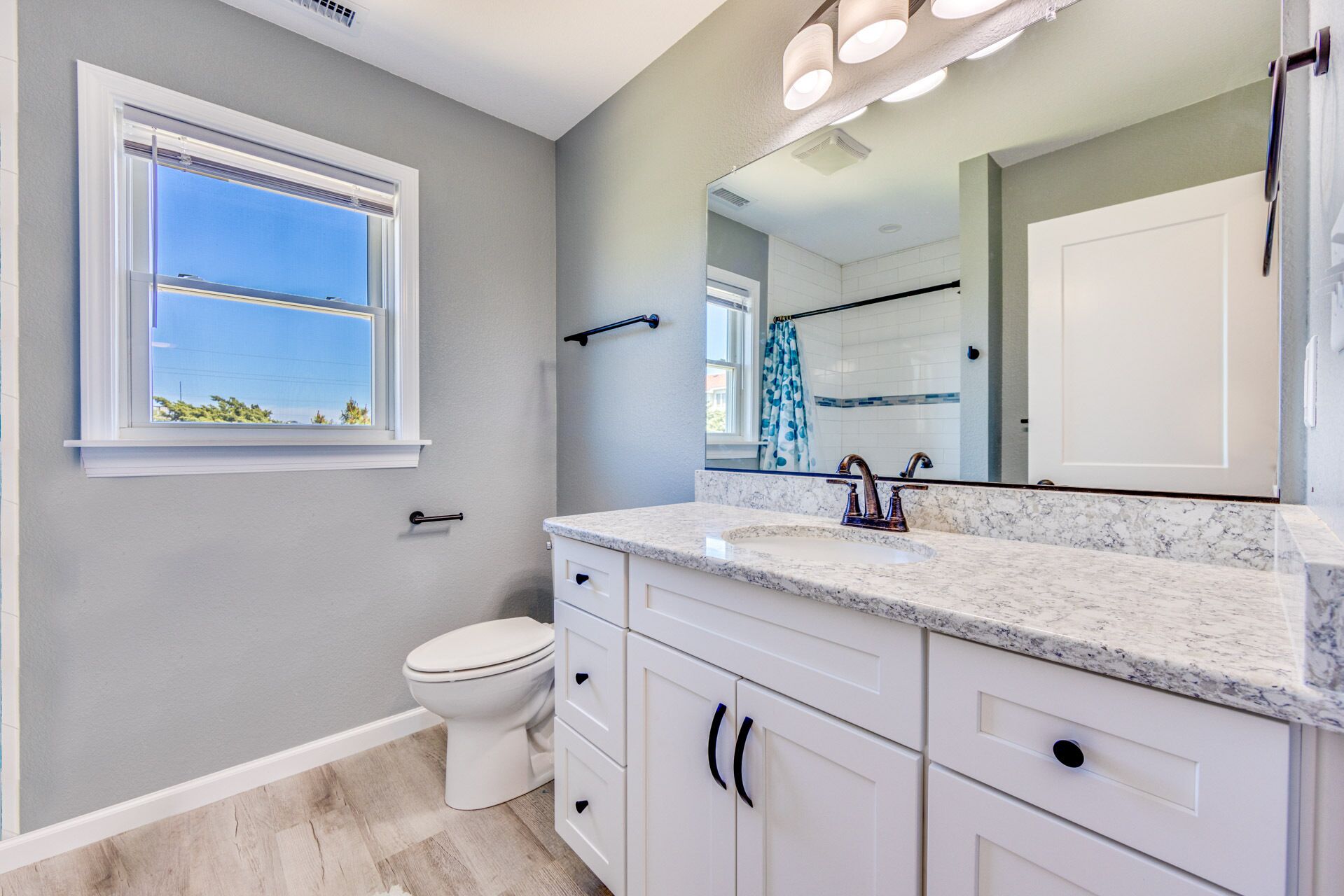 A bathroom with a toilet, a sink with a mirror, and a window with a view of the sky.