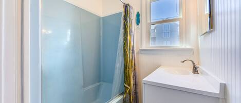 Ein Badezimmer mit Duschkabine aus Glas, Waschbecken und Fenster.