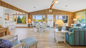 A spacious living area with a high ceiling, wooden walls, and large windows offering a view of the outdoors. - Oceanfront Home with Private Beach Access, Wet Bar, Grill, and Smart TV (Avon)