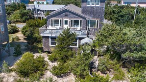 A two-story house with a balcony, surrounded by dense greenery and a clear view of the ocean. - Oceanfront Home with Private Beach Access, Wet Bar, Grill, and Smart TV (Avon)