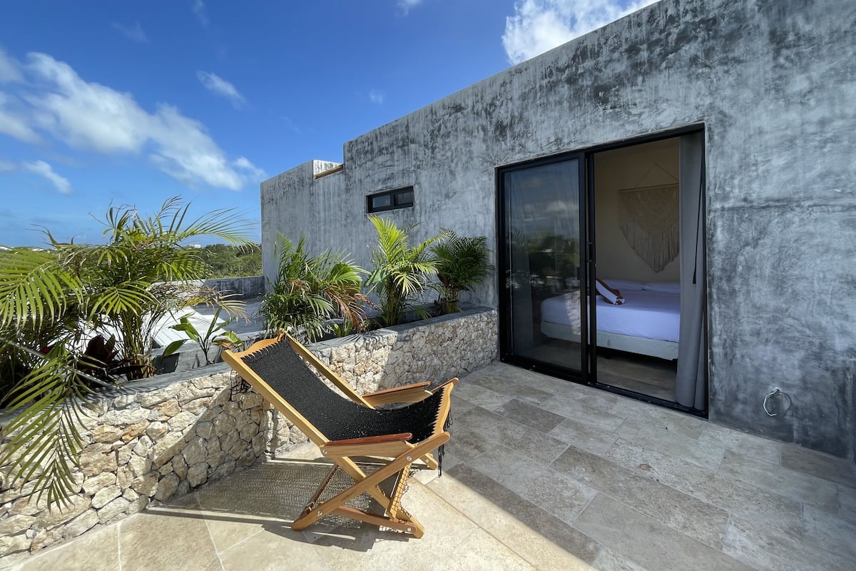 Un área de estar moderna al aire libre con una silla de lounge, un muro de piedra y una cama en una habitación con puerta corrediza de vidrio.