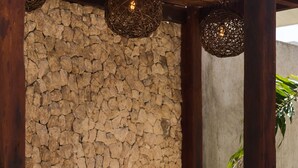 A stone wall, wooden furniture, and lush greenery in a shaded outdoor area. - Xentum Residences - Dreamed Condo (Tulum)