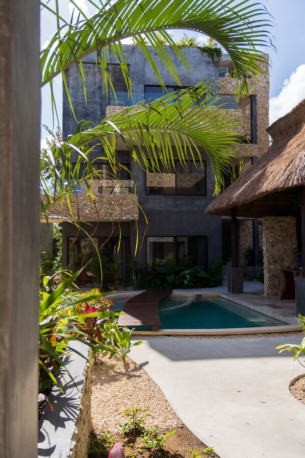 Un edificio moderno con piscina, rodeado de plantas tropicales y una estructura de techo de paja.