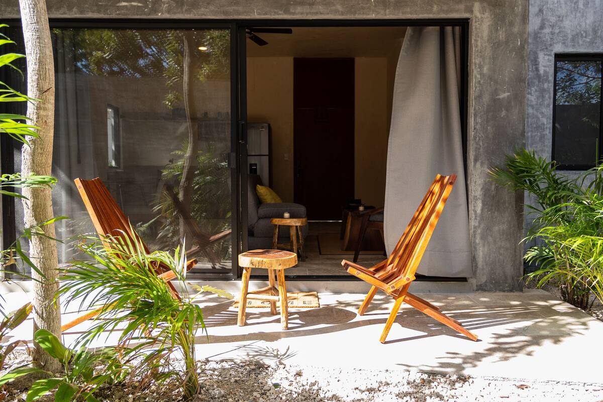 Un espacio al aire libre con una silla y mesa de madera, rodeado de plantas.