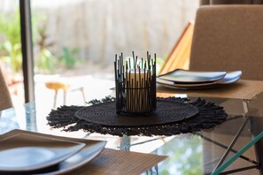 Una mesa de comedor con un centro de mesa de vela, cristalería transparente y un mantel individual.