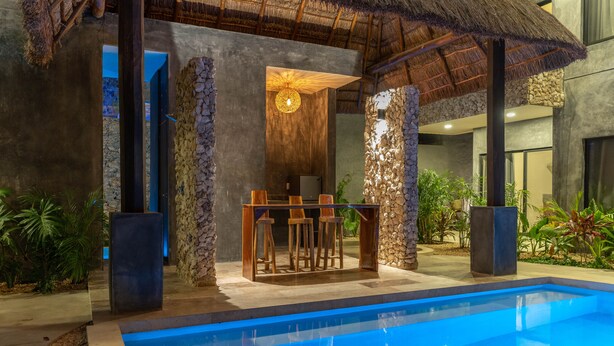 A modern pool area with a bar, stone walls, and tropical plants. - Xentum Residences - Dreamed Condo (Tulum)