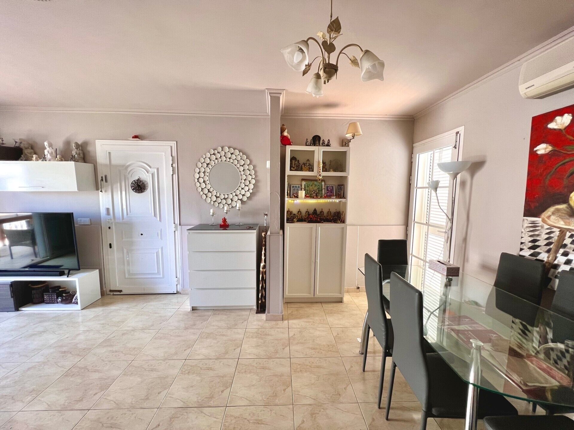 A modern kitchen with white cabinetry, a dining area with a glass table, and a decorative mirror on the wall.