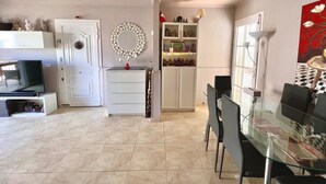 A modern kitchen with white cabinetry, a dining area with a glass table, and a decorative mirror on the wall. - Ganesh House 2 Bedrooms (Tías)