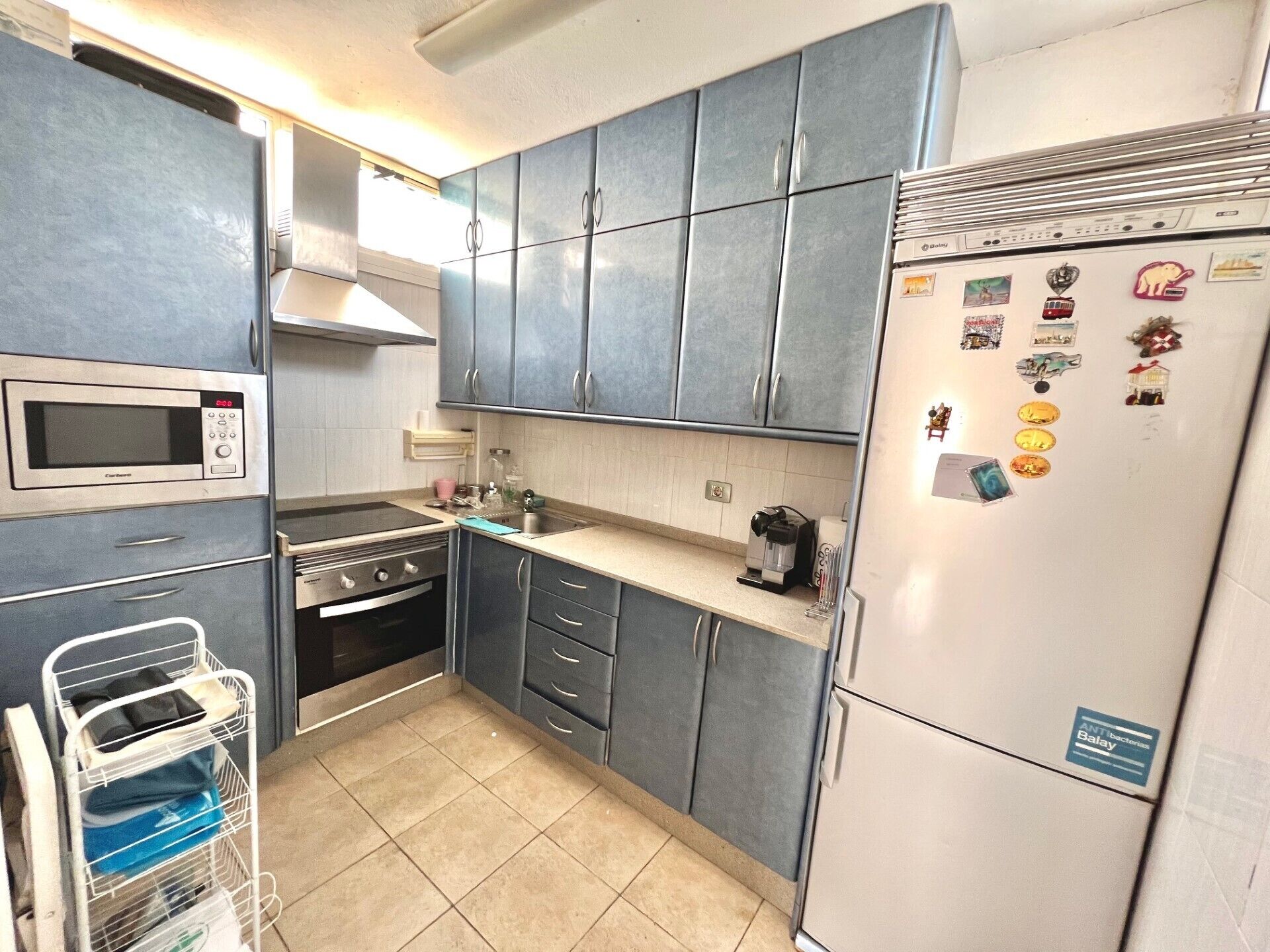 A compact kitchen with grey cabinets, a built-in microwave, a stove, and a refrigerator adorned with magnets.