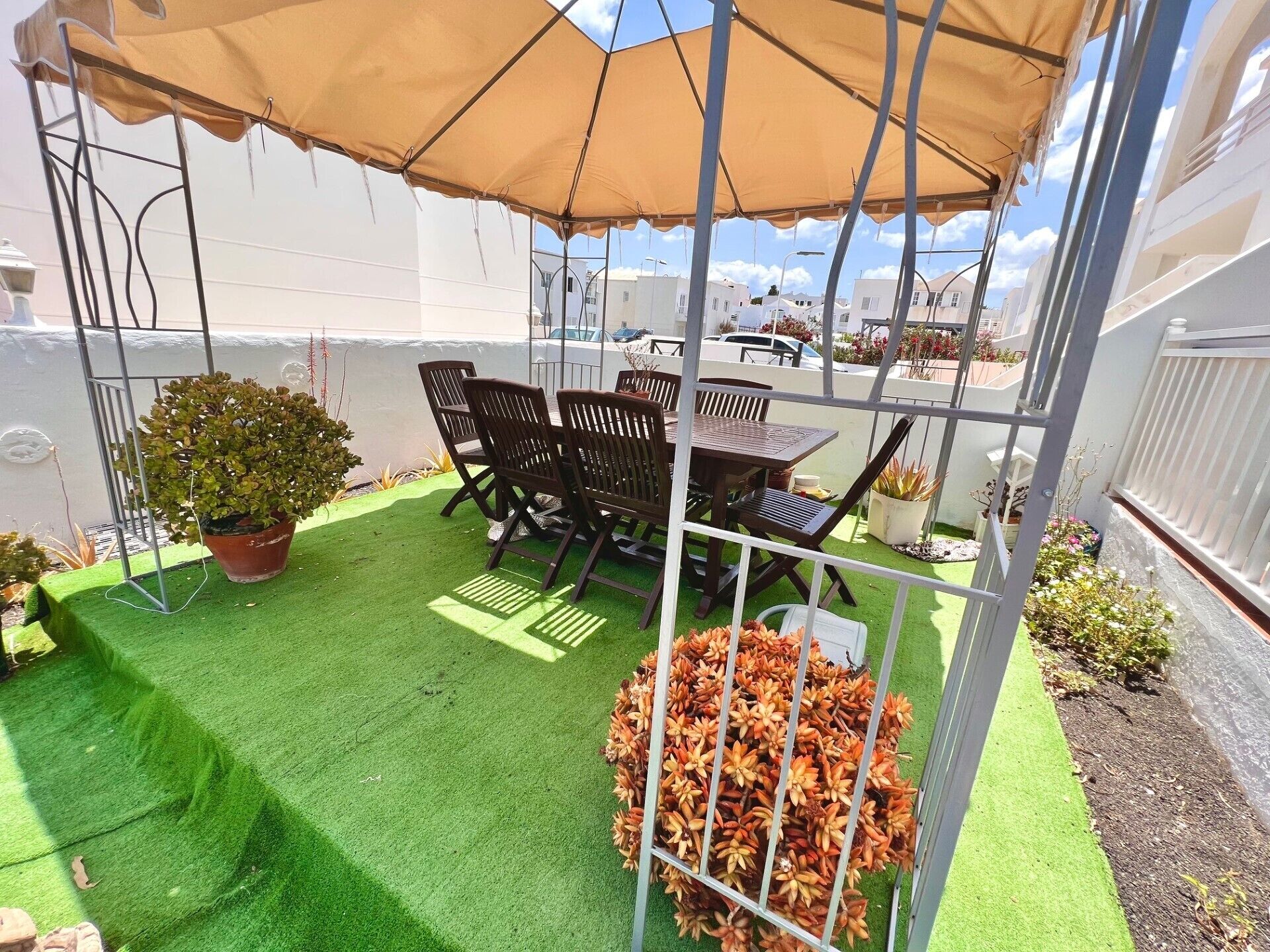 A patio with a table and chairs under a canopy, surrounded by artificial grass and potted plants.