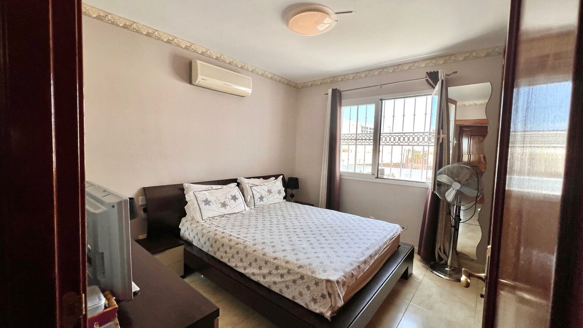 A bedroom with a bed, bedside table, and a standing fan.