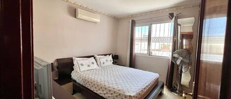 A bedroom with a bed, bedside table, and a standing fan.