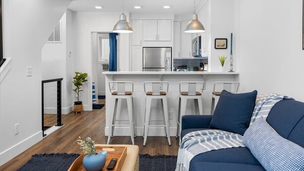 A modern kitchen with white cabinets, a stainless steel refrigerator, and a bar area with white stools.