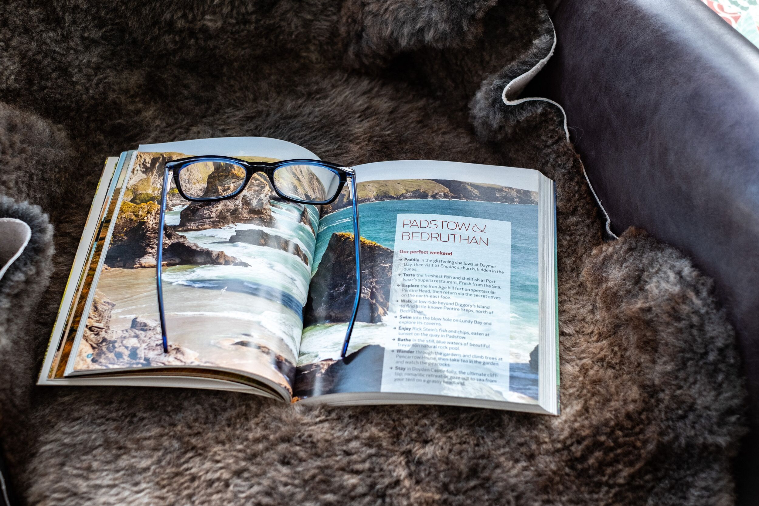 An open travel guidebook with a pair of glasses on top, detailing attractions in Padstow & Bedruthan.