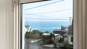 A view through a window of a residential area with a wooden fence, a paved driveway, and a building with a sloped roof. - Seapinks (Port Isaac)