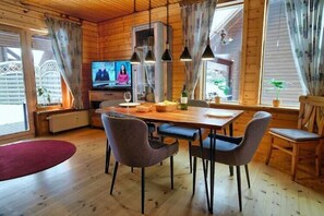 Un intérieur en bois comprenant une table à manger, des chaises, un téléviseur et de grandes fenêtres.