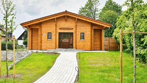 Une cabane en bois avec une allée pavée menant à l’entrée, entourée de verdure.