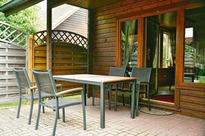 Eine Holzhütte mit einem Patio, einem Tisch, Stühlen, einer überdachten Sitzgelegenheit und einer Tür zu einem Garten.