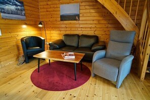 L’intérieur d’une cabane en rondins, avec un plancher en bois, un tapis rouge, une table en bois, un canapé, une chaise et une lampe.