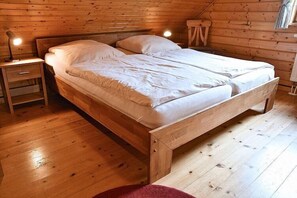 Un lit en bois dans une pièce dont le plafond est en pente, avec une table de chevet et une petite table.