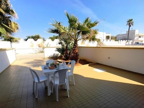 Une terrasse sur le toit, avec une table dressée pour quatre personnes, entourée de palmiers et surplombant un ciel bleu azur.