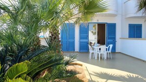 A white building with blue shutters, a patio with white chairs, and palm trees. - Monolocale Torre San Giovanni Verso Sud (Ugento)