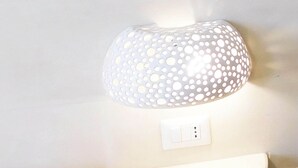 A wall-mounted lamp with a perforated design, a white switch, and a white bedside table in a hotel room. - Monolocale Torre San Giovanni Verso Sud (Ugento)