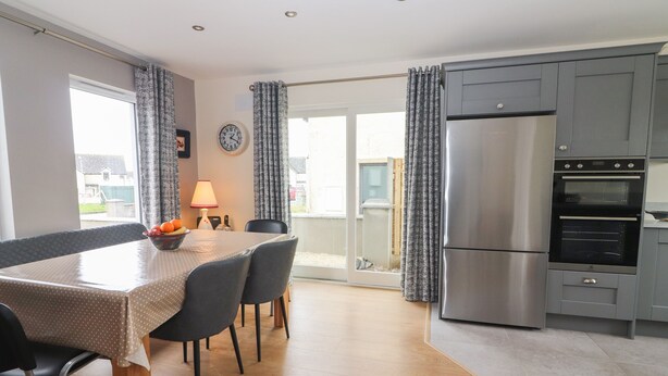 Une cuisine moderne avec des meubles gris, un réfrigérateur en acier inoxydable et un coin repas comprenant une table et des chaises.