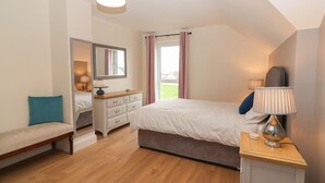 Une chambre à coucher comprenant un lit, une table de chevet, une lampe, une commode, un banc et une fenêtre avec des rideaux.