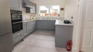 Une cuisine moderne avec des meubles gris, un four double et un petit îlot central doté d’un évier.