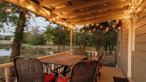 Une terrasse extérieure avec une table et des chaises, des guirlandes lumineuses et une vue sur un lac.