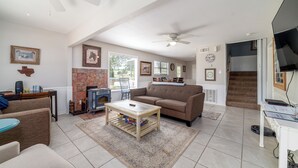 Un salon spacieux avec un canapé marron, une table basse en bois et une cheminée. On y trouve également un ventilateur de plafond, un téléviseur et un escalier menant à un autre niveau.