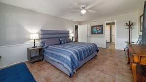 Une chambre à coucher comprenant un lit, des tables de chevet, un ventilateur de plafond et une table à manger.