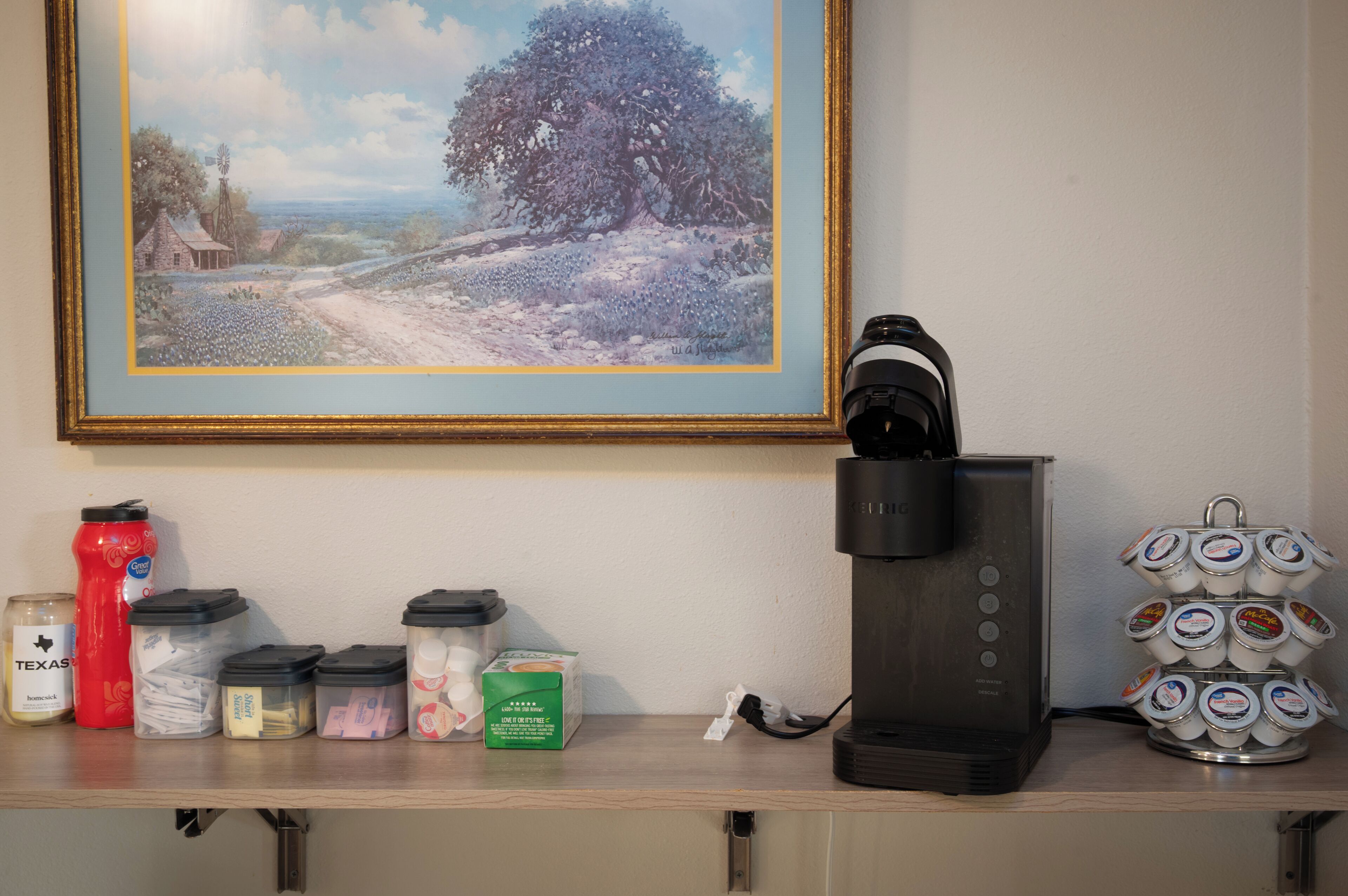 Una cafetera, una botella de agua y recipientes con leche para café sobre una repisa.