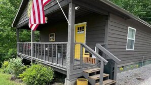 Een houten hut met een gele deur, een veranda met een leuning, en een Amerikaanse vlag.