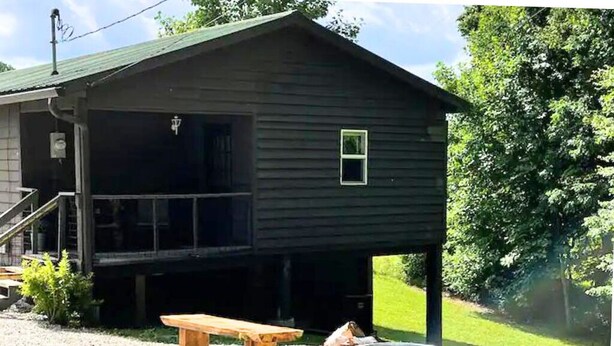 Een houten hut met een veranda, een houten bank en een vuurkorf van steen.