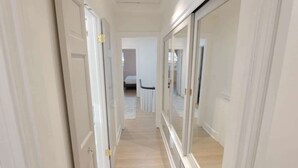 Un pasillo estrecho con puertas blancas y un armario espejado.