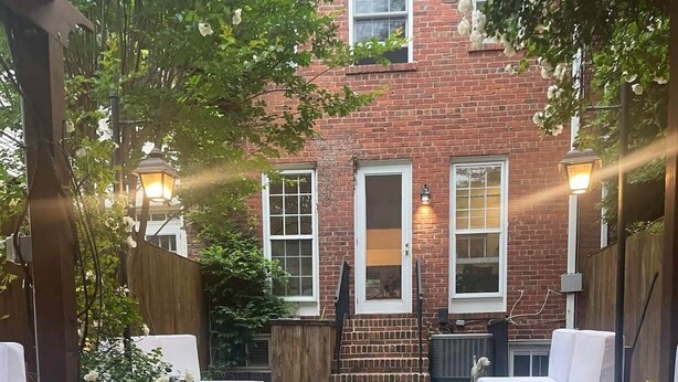 Un patio exterior con un hogar a fuego de ladrillo, una pérgola de madera y un edificio de ladrillo al fondo.