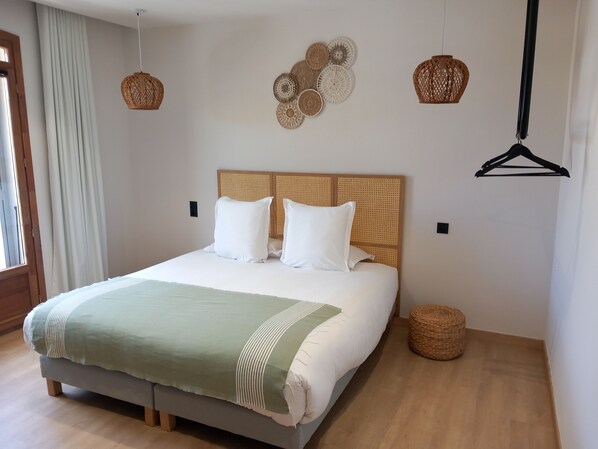 A neatly made bed with a green and white striped blanket, a wooden headboard, and two white pillows. There are two woven baskets on the floor, one on each side of the bed. - Intense Boutik Hôtel (Port-Vendres)