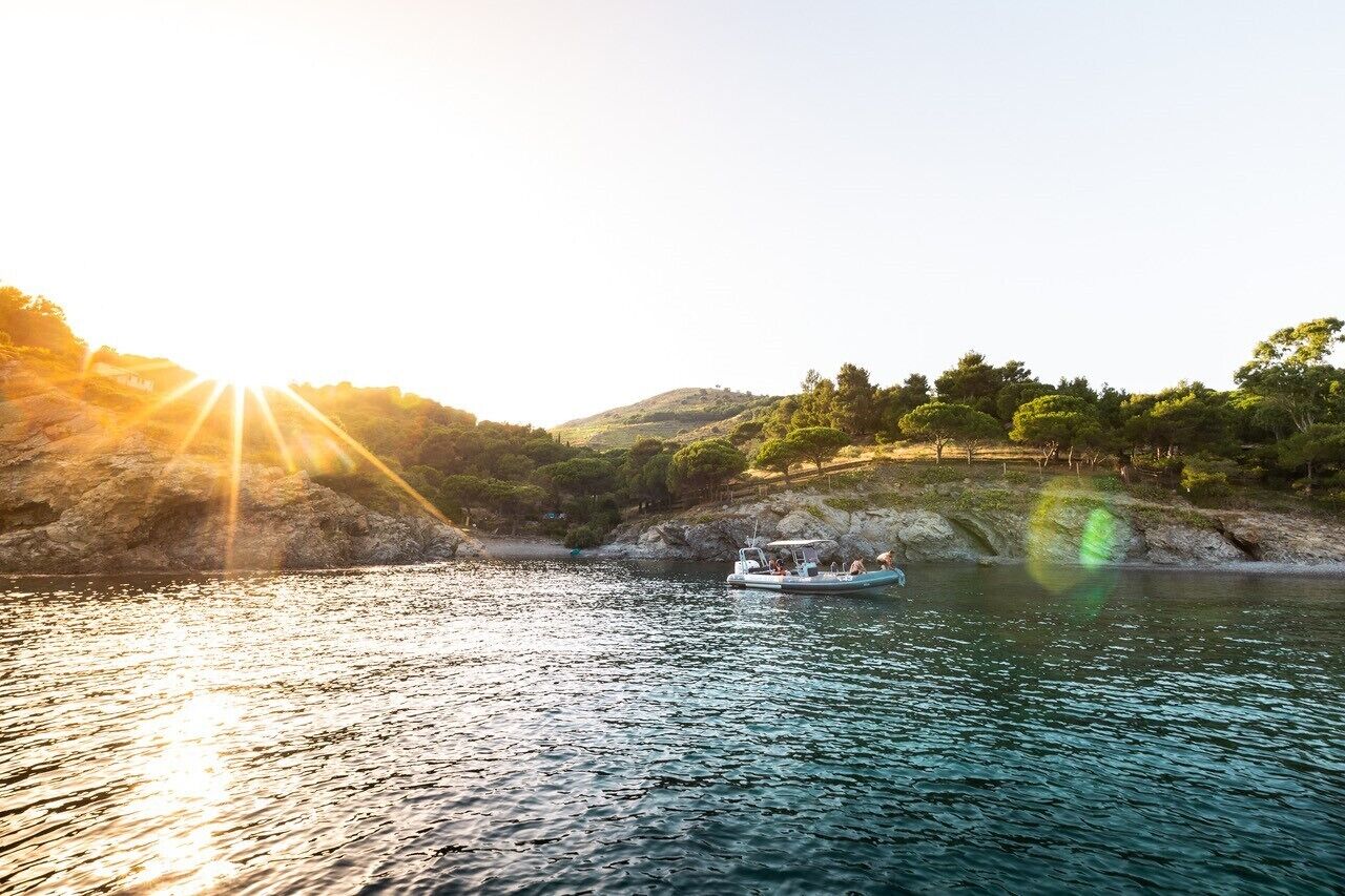 A boat on a calm lake with a rocky shoreline and trees in the background.