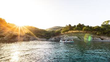 A boat on a calm lake with a rocky shoreline and trees in the background.