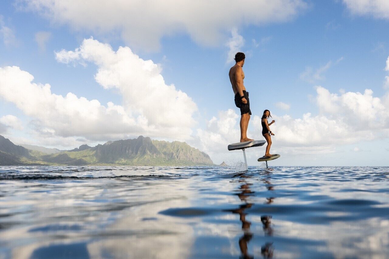 A person standing on a surfboard in the water with mountains in the background.