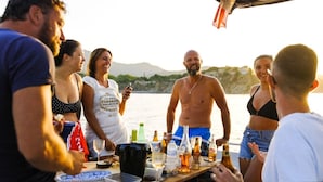 A group of people socializing at a table with various bottles and glasses, set against a scenic waterfront backdrop. - Intense Boutik Hôtel (Port-Vendres)